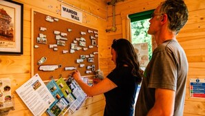 L’intérieur d’un chalet en bois, avec un panneau d’affichage en liège où sont accrochés divers objets et une pancarte sur laquelle on peut lire : « WANDER WALL ».