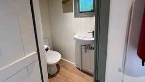 Ett litet, kompakt badrum med en toalett, ett handfat och ett fönster ovanför handfatet.