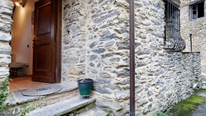 Ein Steinhaus mit einer Holztür, einer kleinen Außen-Sitzgelegenheit und einem Fenster mit einem Metallgeländer.