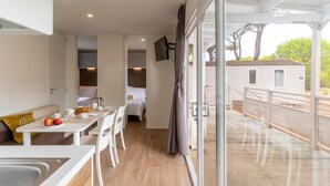 A modern, well-lit room with a dining area, a bed, and a view of a wooden deck and house.