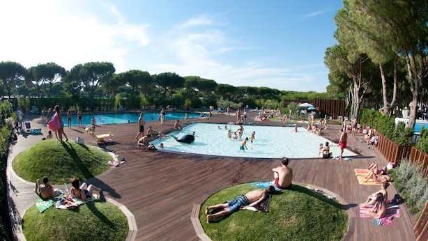 A pool area with multiple swimming pools, sunbathing areas, and a wooden deck.