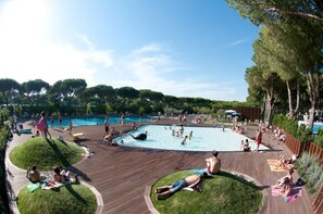 Un área de piscina con varias piscinas, zonas de sol y una terraza de madera.