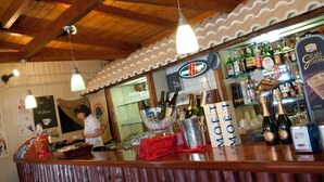 A bar area with a wooden ceiling, hanging pendant lights, and a counter displaying bottles and glasses.
