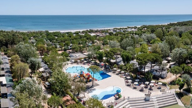 An aerial view of a coastal resort with multiple swimming pools, beach access, and dense greenery.