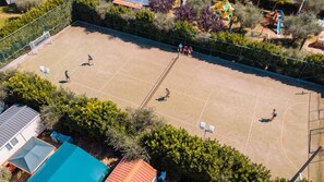 An outdoor basketball court surrounded by trees and a playground.
