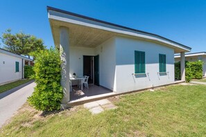 Ein eingeschossiges Gebäude mit überdachter Terrasse, einem kleinen Tisch und Stühlen sowie einer Tür zu einem Innenbereich.
