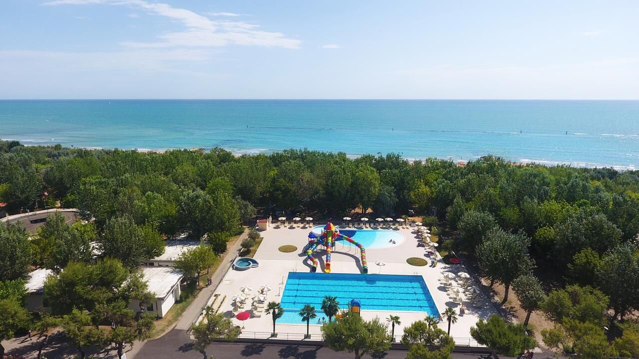 An aerial view of a resort with a large pool, water slides, and a beach.
