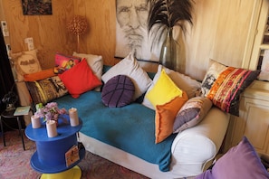 A room with a bed, pillows, a small table with candles, and a wall with a painting.