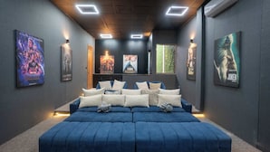 Une salle de cinéma maison moderne, dotée d’un grand canapé d’angle bleu, d’affiches accrochées au mur et d’un éclairage encastré.