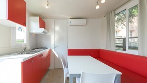 A compact kitchen with red cabinets, a white countertop, and a built-in stove. There is a white dining table with a red bench.