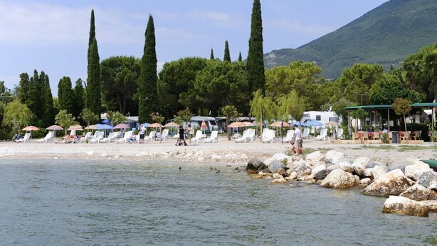 A beach with lounge chairs and umbrellas, a rocky shoreline, and trees in the background.