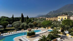 A resort with a large swimming pool, lounge chairs, and a mountainous backdrop.
