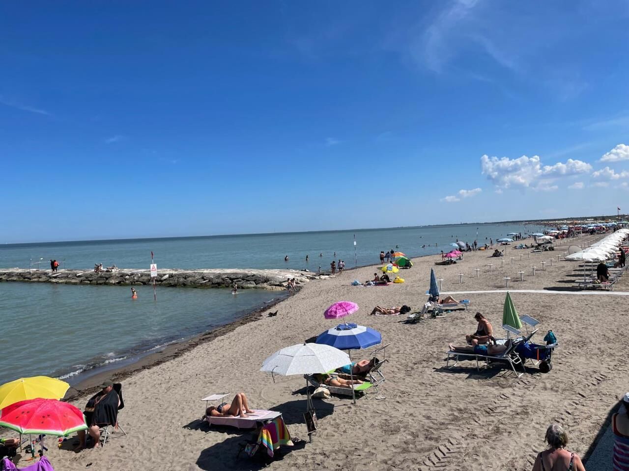 Une plage où l’on peut voir des gens se prélasser au soleil, des parasols et une digue rocheuse.