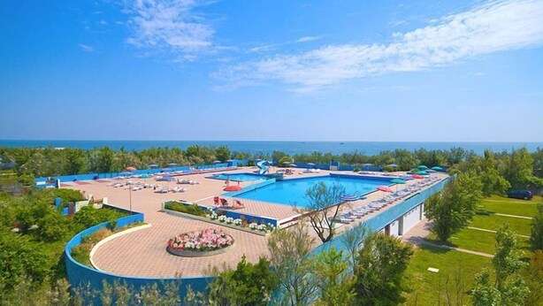 A resort with a large pool, sun loungers, and a view of the sea.