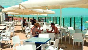 An outdoor dining area with white tables and chairs, large white umbrellas, and a view of the ocean.