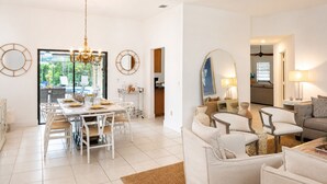 A modern living room with a dining area, white furniture, and a large window. - Beautiful Home with Sauna & Heated Pool-Spa, 5min from Beaches, close to Airport (Lantana)