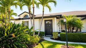 A modern house with a black door, surrounded by tropical plants and a well-maintained lawn. - Beautiful Home with Sauna & Heated Pool-Spa, 5min from Beaches, close to Airport (Lantana)