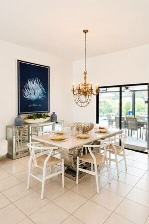 A dining area with a marble table, white chairs, a chandelier, and a large framed artwork on the wall.