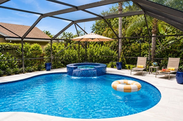 A swimming pool with a hot tub, lounge chairs, and an umbrella.