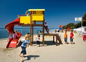 Un parque infantil en la playa con un tobogán y estructuras para escalar.