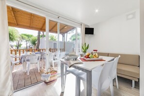 Un comedor luminoso y moderno con terraza de madera, mobiliario blanco y televisor montado en la pared.