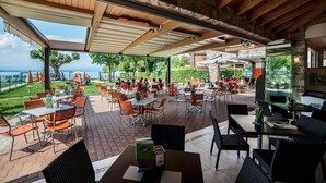 Un área de comedor al aire libre con mesas y sillas, vista al mar y una sección cubierta con pared de vidrio.