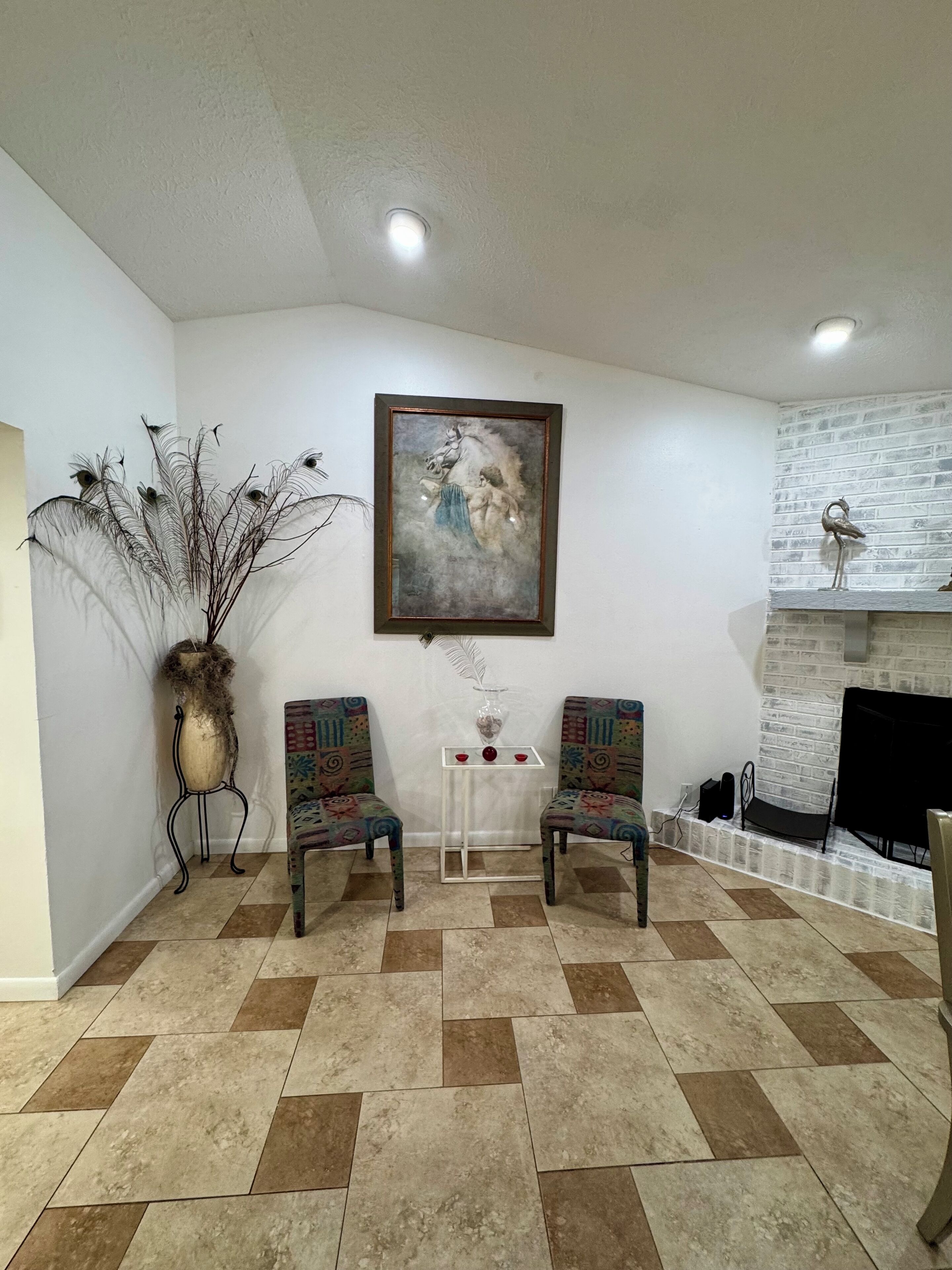 Une pièce avec deux fauteuils à motifs, un tableau, un vase et une cheminée.
