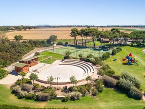 An outdoor amphitheater with tiered seating, surrounded by green lawns and trees.