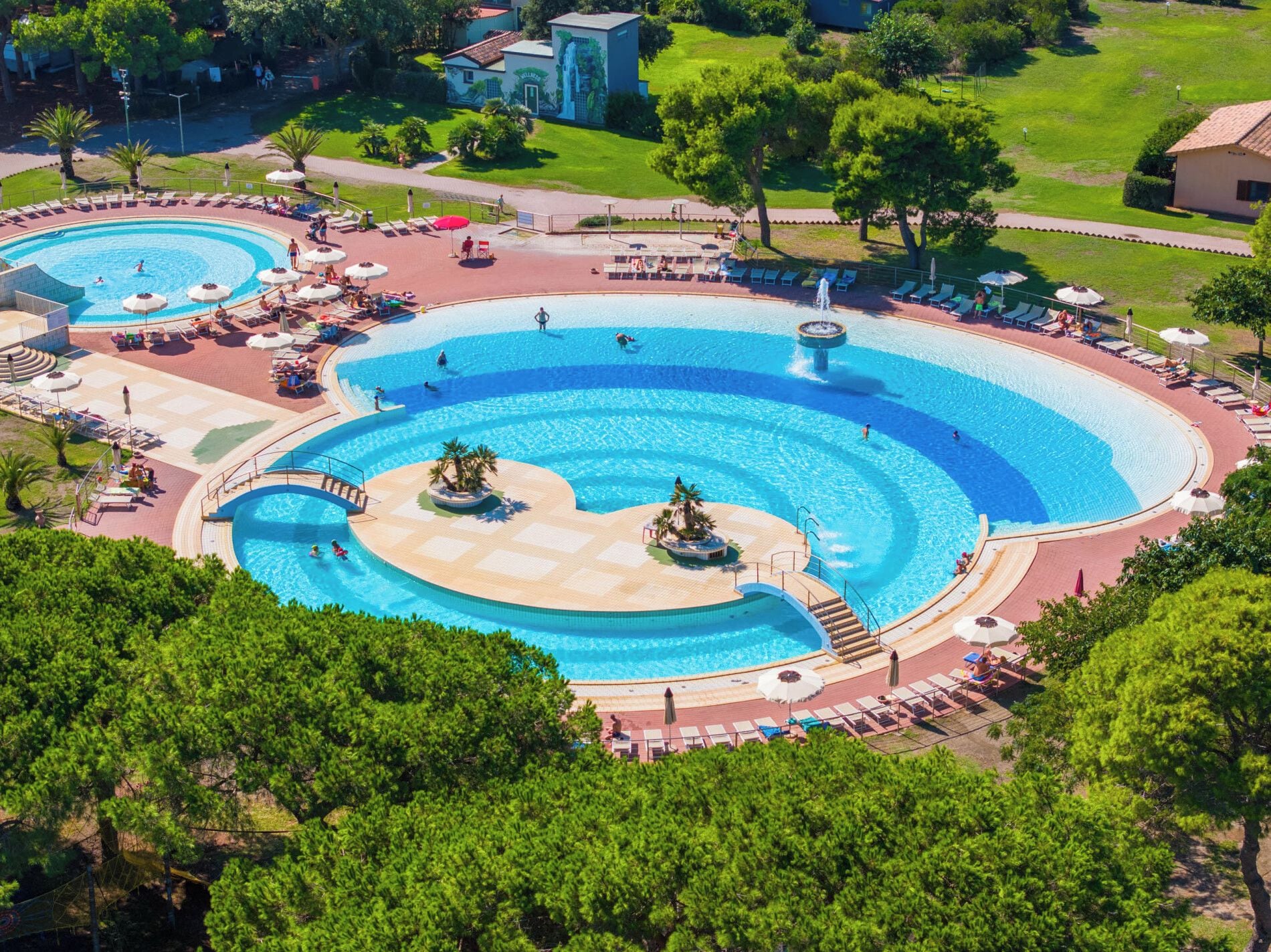 A large outdoor swimming pool with multiple sections and a surrounding deck area with lounge chairs and umbrellas.