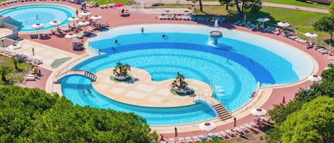 A large outdoor swimming pool with multiple sections and a surrounding deck area with lounge chairs and umbrellas.