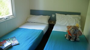 Una habitación con dos camas individuales, una ventana y un peluche sobre una cama.