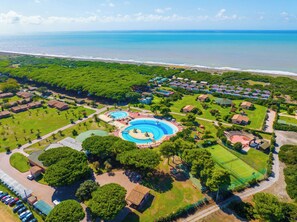 An aerial view of a resort with multiple swimming pools, a tennis court, and a beach.