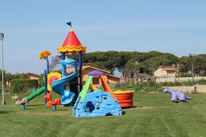 Un parque infantil con toboganes y estructuras para escalar, rodeado de césped y árboles.
