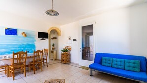 A living room with a blue sofa, wooden chairs, a TV, and a painting on the wall.