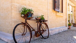 A bicycle with a basket and panniers parked against a building with a stone facade and a window with shutters.