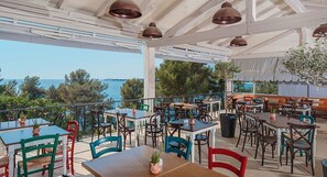 Un espace extérieur aménagé pour les repas, avec des tables et des chaises, donnant sur un plan d’eau.