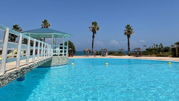 A clear blue pool with a white deck and palm trees in the background. - Ferienanlage Manacore Mobilehome Happy Easy für 6 Personen (Manaccora)