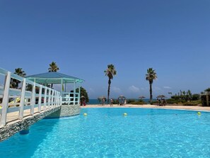 Una piscina azul cristalina con un deck blanco y palmeras al fondo.