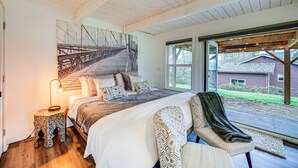 A bedroom with a large bed, a nightstand, a chair, a window, and a painting of a bridge. - Stylish Bellingham Home w/ Lake + Mountain Views! (Bellingham)