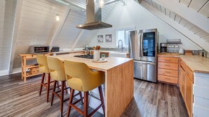 A modern kitchen with a central island, wooden bar stools, stainless steel appliances, and a sloped ceiling with skylight. - Stylish Bellingham Home w/ Lake + Mountain Views! (Bellingham)