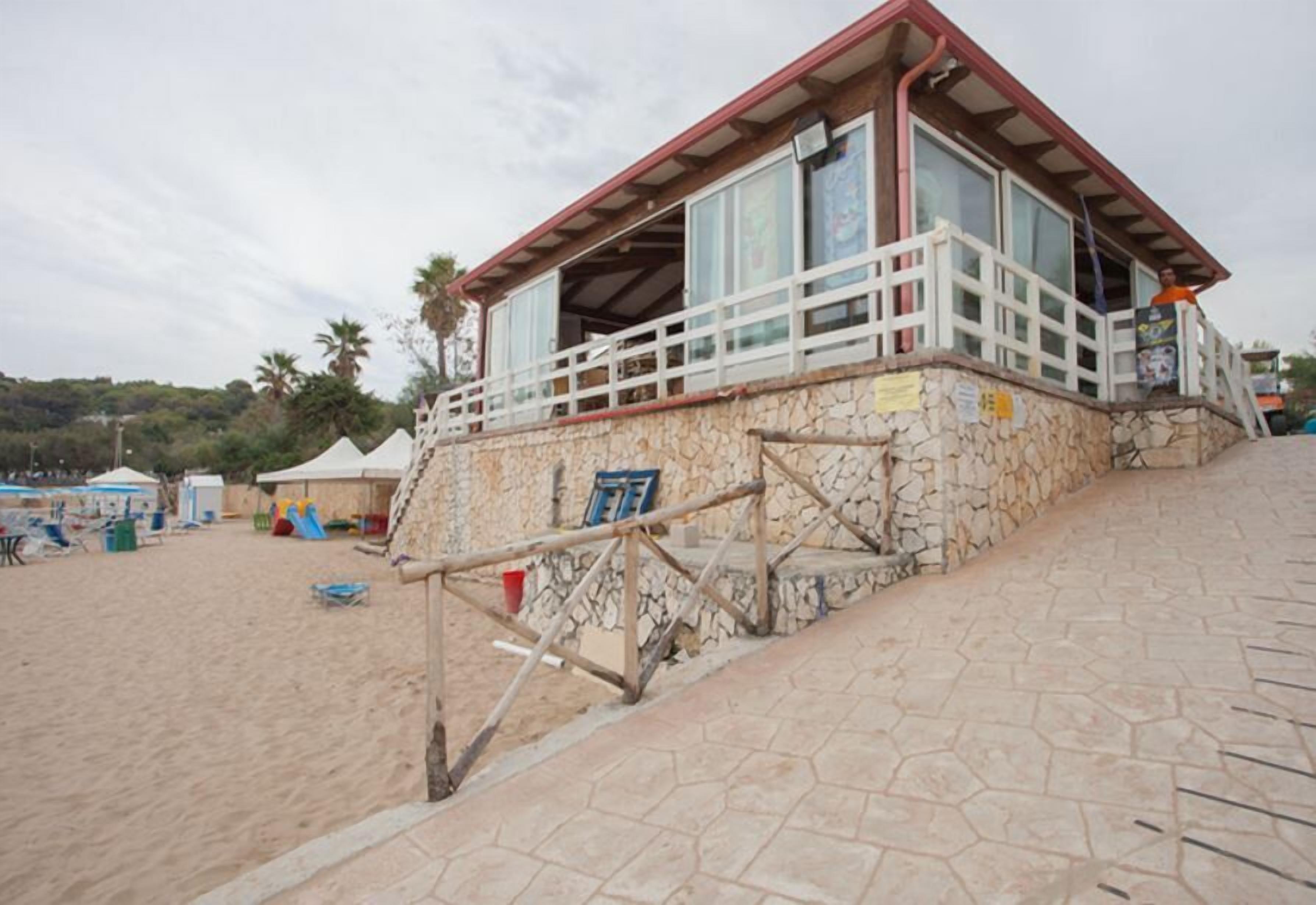 A beachside building with a stone facade, a wooden staircase, and a balcony with a railing.