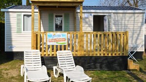 A mobile home with two white plastic lounge chairs in front, a wooden deck, and a sign that reads "Happy Premium."