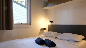 Habitación de hotel con cama, ropa de cama blanca, cabecera, luz fijada a la pared y ventana con cortinas.