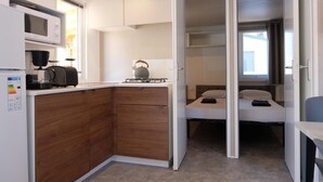 Una kitchenette compacta con microondas, tetera y cafetera. Hay una cama con almohada y una mesita de noche.
