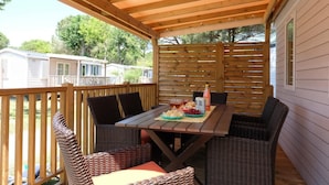 Un patio cubierto con mobiliario de mimbre y una mesa dispuesta para dos, con una bandeja de frutas y bebidas.