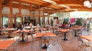An outdoor café with wooden tables and chairs, large windows, and a tiled floor. - Ferienpark Free Time Mobilehome Happy Plus für 7 Personen (Marina di Bibbona)