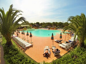 Un espace piscine agrémenté de chaises longues et de parasols, entouré de palmiers.