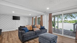 Ein modernes Wohnzimmer mit grauem Sofa, Hocker und einem Flachbildfernseher an der Wand.