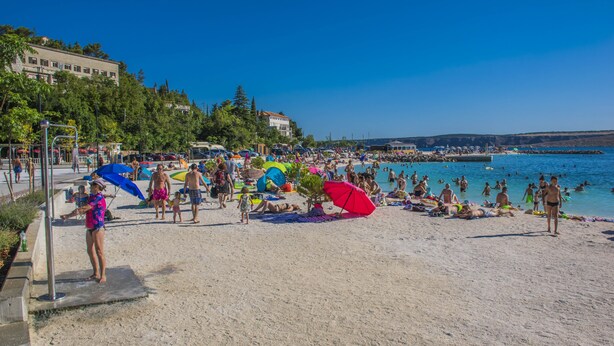 Una playa concurrida, gente tomando el sol y nadando.