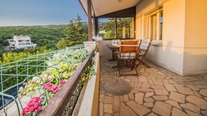 Un balcón con piso de piedra, una mesa con sillas y vistas a vegetación y un edificio a lo lejos.